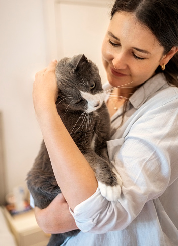 Close-up of a young woman holding her pet cat in her arms while standing at home