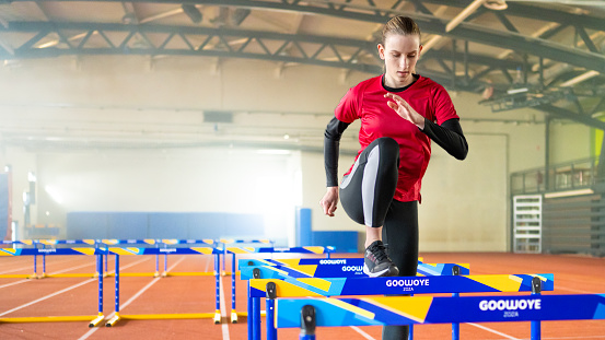 Athlete young woman doing warm-up exercises on hurdle track.