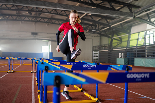 Athlete young woman doing warm-up exercises on hurdle track.