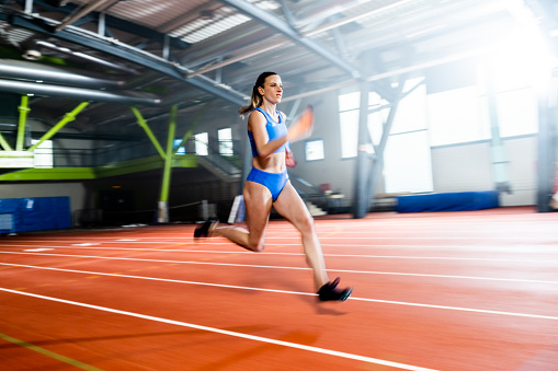 Blurred motion of athlete young woman running on sports track.
