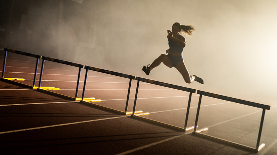 Athlete young woman jumping over hurdles during practice.
