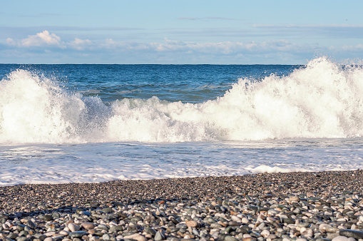 Large sea waves with splashes and foam roll onto a pebble beach. Soft selective focus.