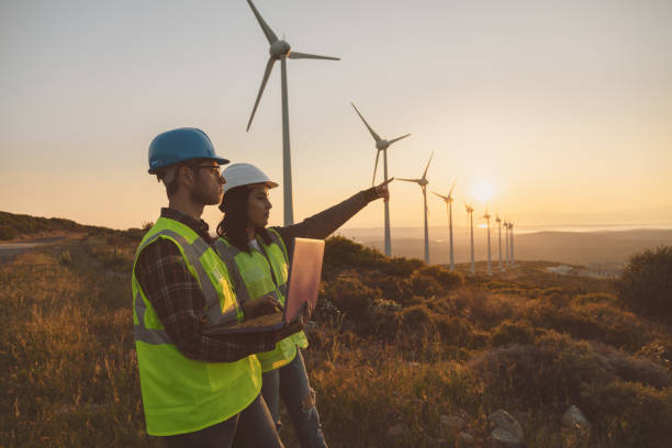 Young maintenance engineer team working in wind turbine farm at sunset stock photo