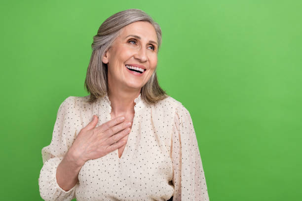 Photo of friendly person with gray hairstyle dressed elegant blouse look empty space palm on chest isolated on green color background stock photo