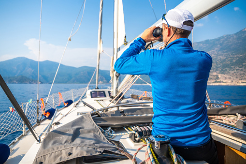 Young man captain on the yacht looking through binoculars during sailing boat control. Travel and active life. High quality photo