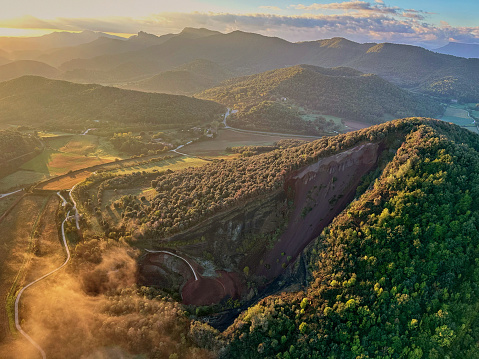 Hot air balloon point of view of sunlight and low-lying fog over Garrotxa volcanic field, part of Volcanic Zone Natural Park. Province of Girona, Spain.