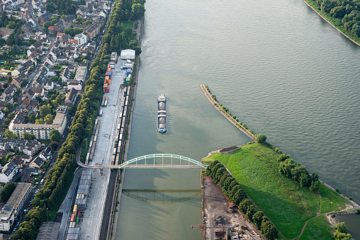 a cargo ship passes the entrance to Niehl port of river Rhine in Cologne. A pedestrian bridge spans the port basin