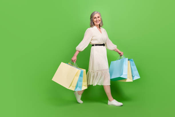 Full length photo of pretty sweet woman dressed beige outfit walking holding bargains isolated green color background stock photo