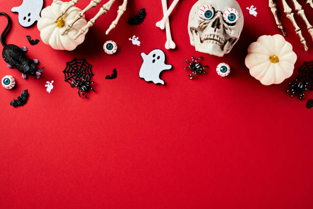 istock Flat lay composition with Halloween holiday decorations on red background. Top view skull with bloody eyes, pumpkins, ghosts, skeleton hands, rat, bats on red background. Happy Halloween holiday 1598273111