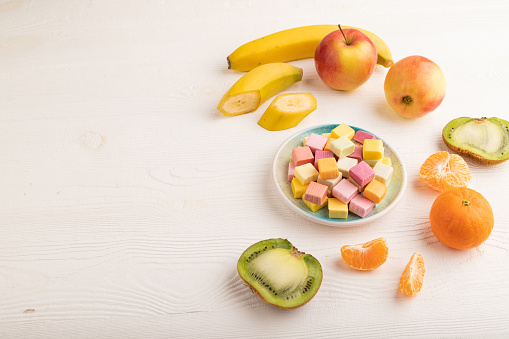 Various fruit jelly chewing candies on plate on white wooden background. apple, banana, tangerine, kiwi, side view, copy space.