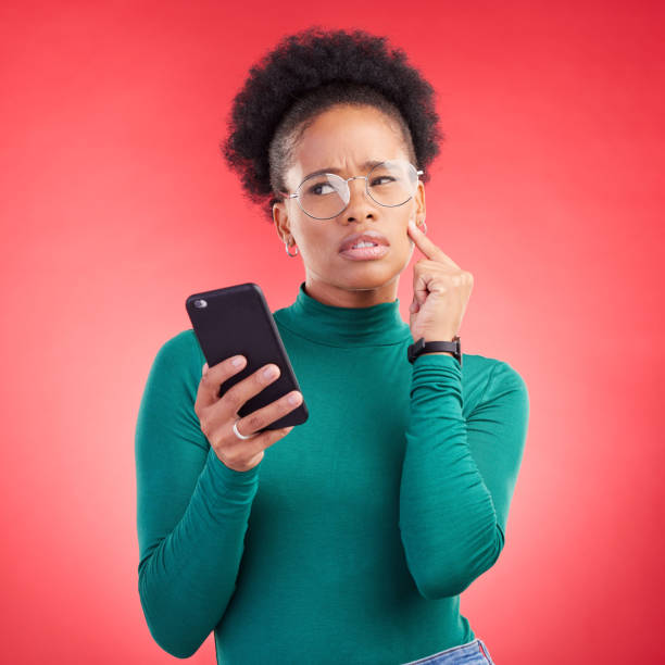 istock Thinking, phone and black woman in studio confused by text, application or how to steps on red background. Doubt, why and African person with questions for scam or spam contact on smartphone 1598311108