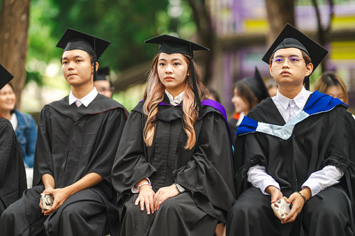 Young Asian graduating class sitting in line waiting to receive diplomas before graduation ceremony.