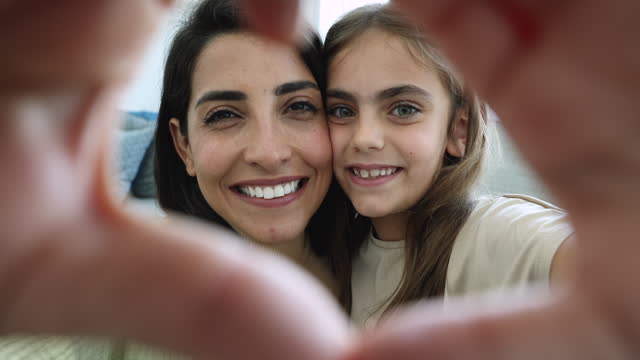 Happy mom and adopted daughter showing love sign, closeup portrait