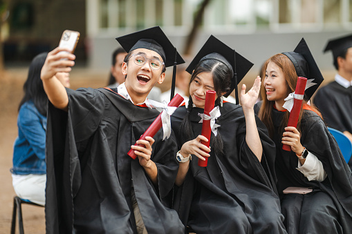Portrait of a group of Asian students taking selfies on graduation day.