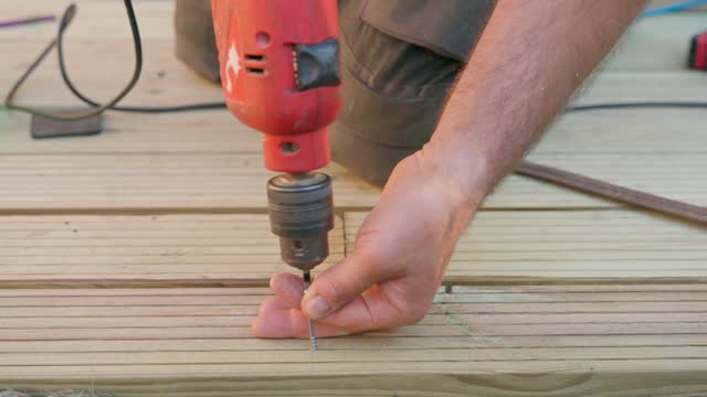 Male builder using drill to unscrew the screws off the timber
