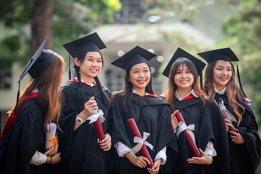A group of young pretty Asian female graduates is celebrating their graduation, smiling while wearing gowns and caps during the graduation ceremony.