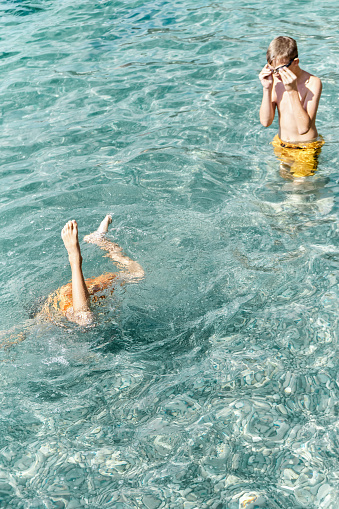 Junior school kid dives into deep transparent blue sea. Couple of brothers enjoys spending summer holidays at seaside playing in water