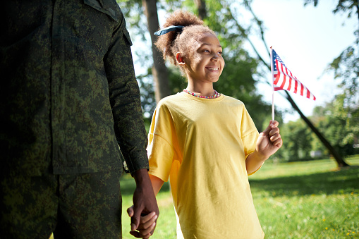 African American little girl with american flag walking with her dad in military uniform outdoors