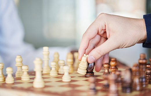 Playing, board game and chess checkmate with a man at a table while moving piece for strategy or challenge. Hands of a male person to play, relax and bond while moving icon for problem solving or win