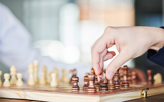 Chess, board game and hand of a man playing at a table while moving piece for strategy or checkmate. Person with wooden icon to play, relax and bond or problem solving and battle in competition