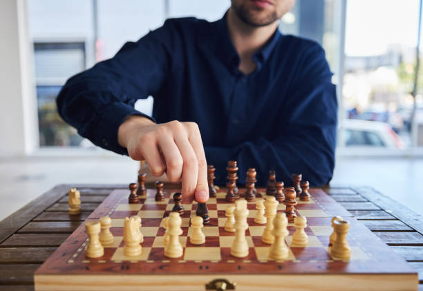 istock Chess, man moving a knight and game of strategy, problem solving or person playing on chessboard in competition. Planning, choice and hand on piece or king, queen and player thinking of winning move 1598386823