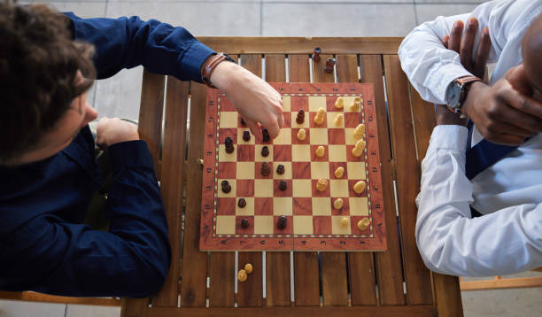 istock Chess, board game and business men playing at a table from above while moving piece for strategy. Male friends together to play, relax and bond with icon for problem solving, challenge or checkmate 1598386841