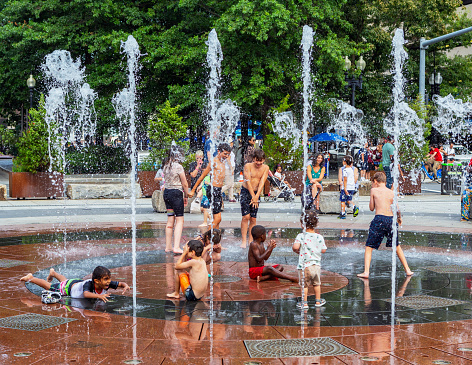 Boston, Massachusetts, USA - August 5, 2023: Rose Fitzgerald Kennedy Greenway's Wharf District Park. This park connects Faneuil Hall and the Financial District with Boston Harbor. Children playing in the Rings Fountain's vertical water jets. The Rose Fitzgerald Kennedy Greenway is a linear park located in several Downtown Boston neighborhoods. It consists of landscaped gardens, promenades, plazas, fountains, art, and specialty lighting systems that stretch over one mile through Chinatown, the Financial District, the Waterfront, and North End neighborhoods.