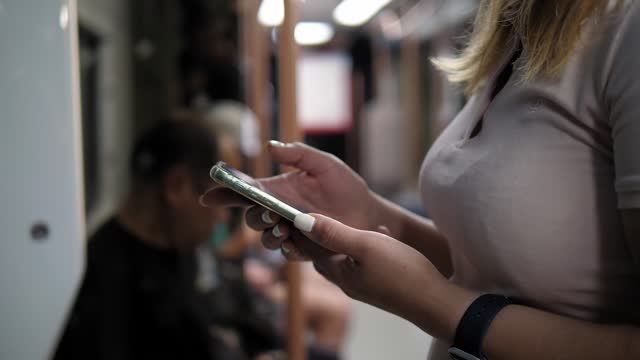 Hands of a woman using a smartphone in a train car in the subway close-up.
