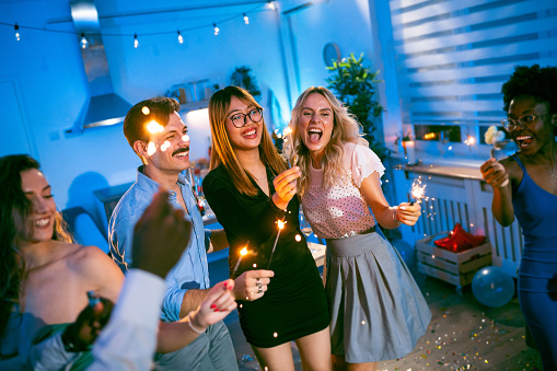 Group of multiracial young female and male people/friends, celebrating New Year's Eve at the house party with sparklers