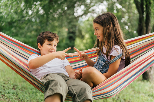 Children playing Rock Paper Scissors game sitting on a hammock in the yard