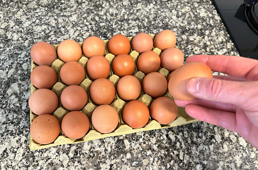 Chicken egg in hand. Natural organic eggs in cardboard package on table in kitchen. 24 eggs in pack box. Eggs for breakfast. Cooking an omelet and scrambled eggs from a chicken egg.
