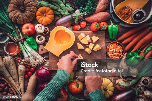 istock Woman chopping squash on a table full of fresh autumnal vegetables 1598445478