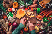 Woman chopping squash on a table full of fresh autumnal vegetables