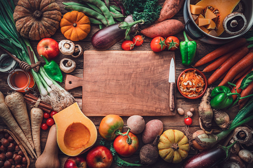 Empty cutting board at the center of fresh organic autumnal vegetables background. Copy space