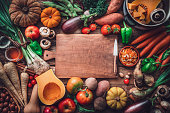 Empty cutting board at the center of fresh organic autumnal vegetables background. Copy space