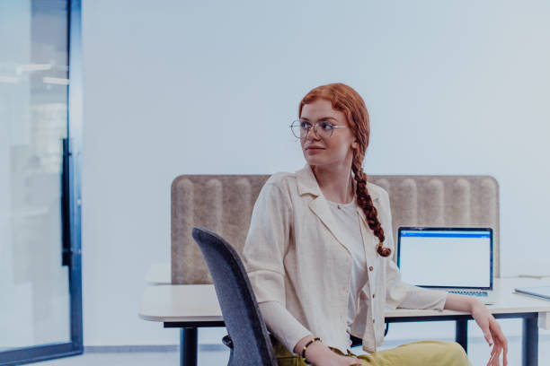A modern businesswoman with striking orange hair sitting confidently in a contemporary office, accompanied by her laptop, embodying professionalism, creativity, and success in a technology-driven workplace una mujer de negocios moderna con llamativo cabello naranja sentada con confianza en una oficina contemporánea, acompañada de su computadora portátil, que encarna el profesionalismo, la creatividad y el éxito en un lugar de trabajo impulsado por la tec