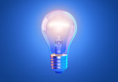 Transparent tungsten glowing light bulb with shining light, isolated on blue background