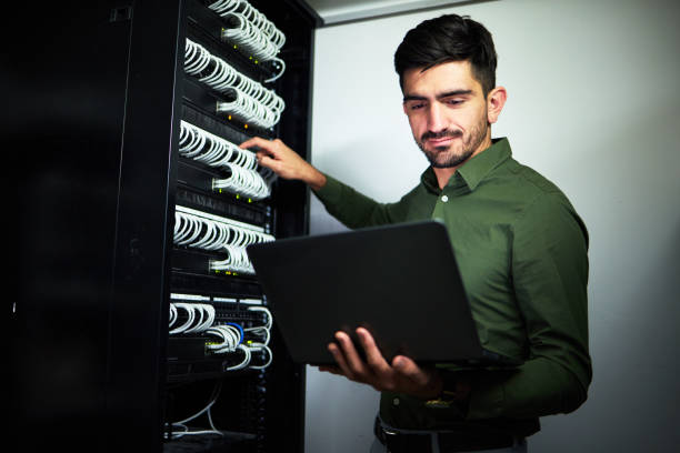 istock Laptop, engineering and man technician in a server room for technical repairs by a control box. Technology, maintenance and professional male electrician working on computer for cybersecurity system. 1598575330