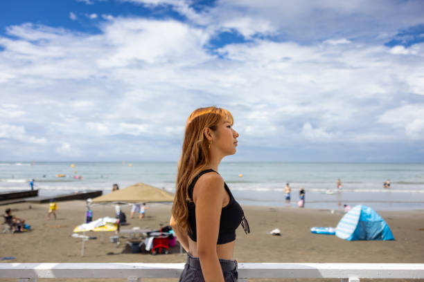 Asian gen-z traveler woman in a white dress enjoys the view to Mykonos island, Cyclades, Greece 2023