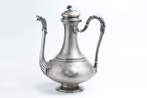 Vintage silver jug lamp teapot on a white background. Antique metal vessel with spout and handle side view. East tableware.