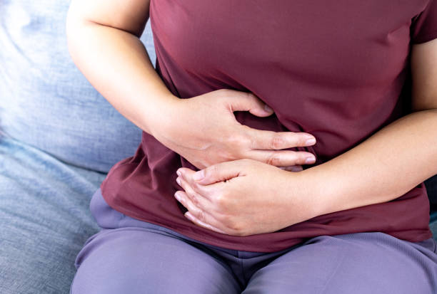 Fat woman having painful stomach ache. eating on time due to wanting to control weight on sofa in the living room, Chronic gastritis. Stomach or menstrual cramps. Health problem Inflammation in body stock photo