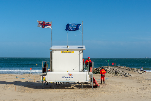 Poole, UK - April 10th 2023: RNLI Lifeguards around the lifeguard tower on Sandbanks Beach.