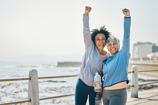 Success, women and friends, fist pump and fitness goals with running outdoor, winning and health. Happy senior female people, exercise achievement while training for marathon with cheers at beach