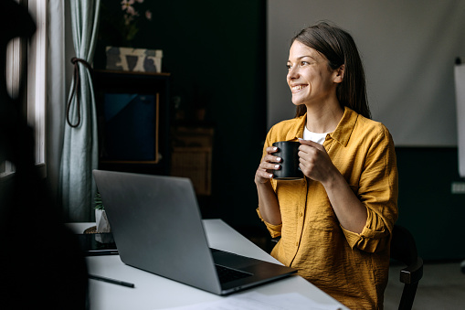 Young smiling beautiful woman enjoying coffee while working at home office