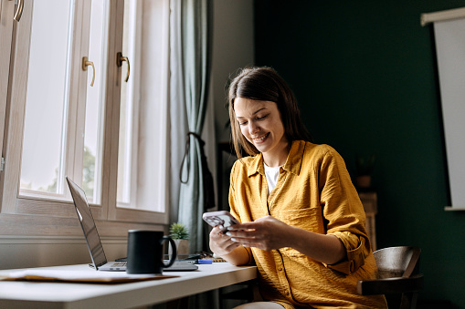 Young smiling woman text messaging while working at home office