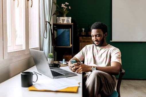 Young casually clothed man text messaging while working at home office