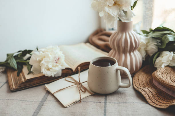 istock Cup of tea, straw hat, open book and peonies, spring still life 1598691888