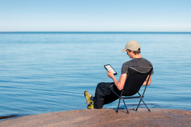 istock A man is reading an e-book on the seashore sitting in a camping chair. 1598694720