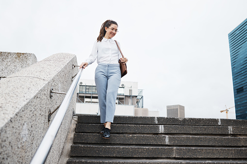 Woman, worker and walking on city building steps happy, smile and cheerful while traveling. Travel, walk and female person smile for commute, leaving and enjoying solo trip in New York outdoor