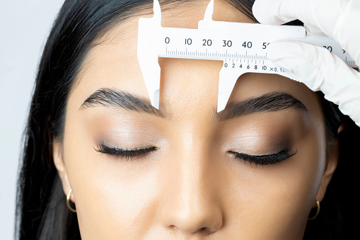 Taking measurements of the young woman's face and eyebrows with a scalimeter to make her eyebrows.
